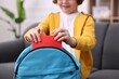 © New Africa - Boy packing his backpack for school on sofa at home, closeup