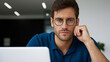 © Tetyana - Young man with a serious expression and eyeglasses focused on his work during a busy day, deeply engrossed in complex thoughts and decision making at a contemporary office, copy space