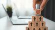 © alex - Achieving your goals by stacking wooden blocks to build a pyramid with a target on the top block and a person's hand placing it on top