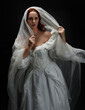 © faestock - close up portrait female model wearing antique white historical ghost bride wedding dress gown, ethereal bridal veil head covering. Isolated standing figure, dark studio background overhead lighting