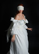 © faestock - close up portrait beautiful female model wearing antique white historical ghost bride wedding dress gown, a veiled mask blindfold covering face. isolated figure on dark studio background, hand gesture
