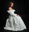 © faestock - Full length portrait beautiful female model wearing antique white historical ghost bride wedding dress gown. classical elegant sitting pose, Isolated figure on dark studio background