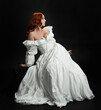 © faestock - Full length portrait beautiful female model wearing antique white historical ghost bride wedding dress gown. classical elegant sitting pose, Isolated figure on dark studio background