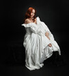 © faestock - Full length portrait beautiful female model wearing antique white historical ghost bride wedding dress gown. classical elegant sitting pose, Isolated figure on dark studio background
