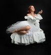 © faestock - Full length portrait beautiful female model with red hair wearing a antique white historical ghost bride wedding dress gown. classical elegant sitting pose, Isolated figure on dark studio background