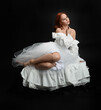 © faestock - Full length portrait beautiful female model with red hair wearing a antique white historical ghost bride wedding dress gown. classical elegant sitting pose, Isolated figure on dark studio background