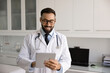 © fizkes - Digital healthcare professional. Smiling male doctor in white hospital coat use electronic pad in clinic office review medical records therapy plans lab results contact with patient via telehealth app