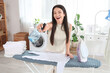 © Pixel-Shot - Beautiful young happy woman with spray bottle, iron and stack of clothes on board in bathroom