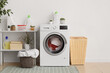 © Pixel-Shot - Modern washing machine, shelving unit and laundry baskets near white wall in room