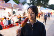 © leungchopan - Woman eating corn dog at night market