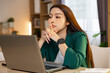 © 220 Selfmade studio - Stressed young Asian business woman looking at laptop screen feeling tired and thoughtful while working at home office desk with serious expression