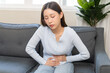 © KMPZZZ - Sick asian young woman in pain, hand holding belly, stomach pain from food poisoning, girl hurt abdomen ache and digestive problem, gastritis or diarrhea. Health care inflammation, abdominal problem