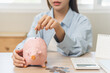 © KMPZZZ - Saving money wealth concept, asian young business woman hand putting coin into piggy for saving cost, cash finance planning to spend enough money on her income for save money, payment tax, investing.