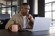 © wavebreak3 - African american man sitting at desk in office working on laptop with coffee