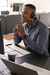 © wavebreak3 - African american man talking by headset, gesturing at office desk monitor with coffee, copy space