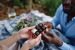 © Milos - An intimate moment captured of a couple happily sharing a box of assorted chocolates while enjoying a picnic in a lush outdoor setting, full of romance and connection.