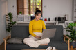 © Wasana - Young asian woman using laptop while relaxing on sofa at home