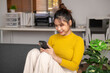 © Wasana - Young woman using smartphone on sofa at home office