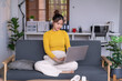 © Wasana - Young asian woman working from home on laptop while sitting on sofa