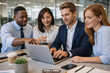© YuTaus - Group of four diverse business professionals collaborating on a laptop at a modern office table with coffee cups and stationery visible in a bright workspace