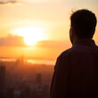 © Shahbaz - A person is seen from behind watching the sun set over a distant landscape, with warm golden light surrounding the figure and soft haze in the background.