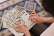 © H_Ko - Fingers grasp crisp bills while a calculator sits ready for use on a soft rug. The atmosphere is calm, focusing on careful budgeting and financial planning in a warm setting.