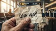 © peacefy - A hand holds a crumpled piece of paper with ONE WAY written on it, set against the backdrop of a busy airport departure lounge, hinting at a journey with no return.