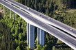© AmazingAerialAgency - Aerial view of the towering bridge slicing through the verdant forest, cars speeding on the asphalt, contrasting with the lush green landscape, Wolfsberg, Carinthia, Austria.