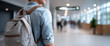 © perfectlab - Young man wearing a backpack standing in a modern, bright indoor public space with blurred people in the background