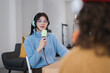 © Studio Marmellata - A young woman wearing headphones and glasses speaks into a microphone while recording a podcast with another person.
