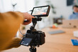 © Studio Marmellata - A person's hand adjusts a camera monitor, capturing a scene with a person working on a laptop in the background.