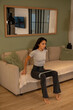© sutulastock - Fit woman performing seated resistance band exercise on sofa at home living room, controlled posture showing lower body activation, stability, rehabilitation and functional indoor fitness training