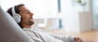 © Alexander - premium commercial stock photo banner of a relaxed man in headphones sitting in a lounge chair listening to music at home, modern bright minimal interior, soft natural daylight, su