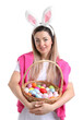 © New Africa - Easter celebration. Smiling woman in headband with bunny ears and wicker basket full of painted eggs on white background
