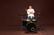 © New Africa - Smiling teenage boy with drumsticks and drum kit on brown background, space for text
