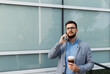 © Novak - Busy businessman in a formal suit talking on a smartphone and holding a takeaway coffee cup