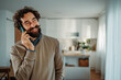 © Dusan - Man smiling enjoying phone call in kitchen