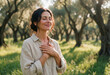 © Kaluya Stock - Smiling woman with closed eyes and hands on her chest in a sunlit olive grove, embodying gratitude, peace, and mindfulness