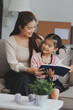 © ARMMY PICCA - A cheerful Asian mother helps her young daughter do homework and color a book at home, while the father works on a laptop in the background. A cozy, bright, and modern family lifestyle.