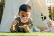 © Kunlathida - Asian child playing observing plants with a magnifying glass lying down in teepee tent