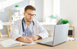 © Studio Romantic - Focused serious young male doctor in white uniform working online on computer, medical knowledge, giving professional consultation, patient distantly in clinic office, diagnostic treatment learning