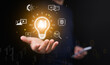 © OleCNX - Artificial intelligence concept. Man with smartphone holding glowing AI lightbulb surrounded by icons of everyday application. Technology solution, creative innovation, prompt generation, smart idea.