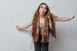 © SHOTPRIME STUDIO - Young woman with long braided hair wearing casual jacket and top posing with arms outstretched making playful expression against plain gray background indoors.