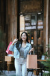 © Natthawadee - Happy Asian woman holding shopping bags outdoors in a trendy urban area, smiling confidently after shopping, representing modern lifestyle, retail experience, and consumer happiness.