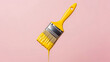 © Vertstyle - A paint brush dripping yellow paint is suspended against a light pink background