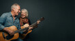 © small, slow, grow - Cheerful senior couple playing acoustic guitars and laughing together against a dark background