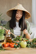 © sofiko14 - A young Asian woman wearing a conical hat enjoys a fresh salad with chopsticks, surrounded by healthy ingredients