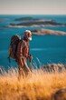 © rabbit75_fot - Explore adventure outdoor in National Park. A man with a backpack standing atop a grassy hill, gazing out over a tranquil body of water. The sky is a clear blue.