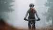 © rabbit75_fot - Cardio sports cycling biking exercise training, healthy lifestyle. A woman mountain biker wearing a helmet, goggles, gloves, and a jacket, riding a bicycle on a misty trail surrounded by trees.