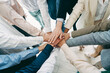 © deagreez - Group of people placing their hands together in a stacked gesture symbolizing teamwork and collaboration in a workplace